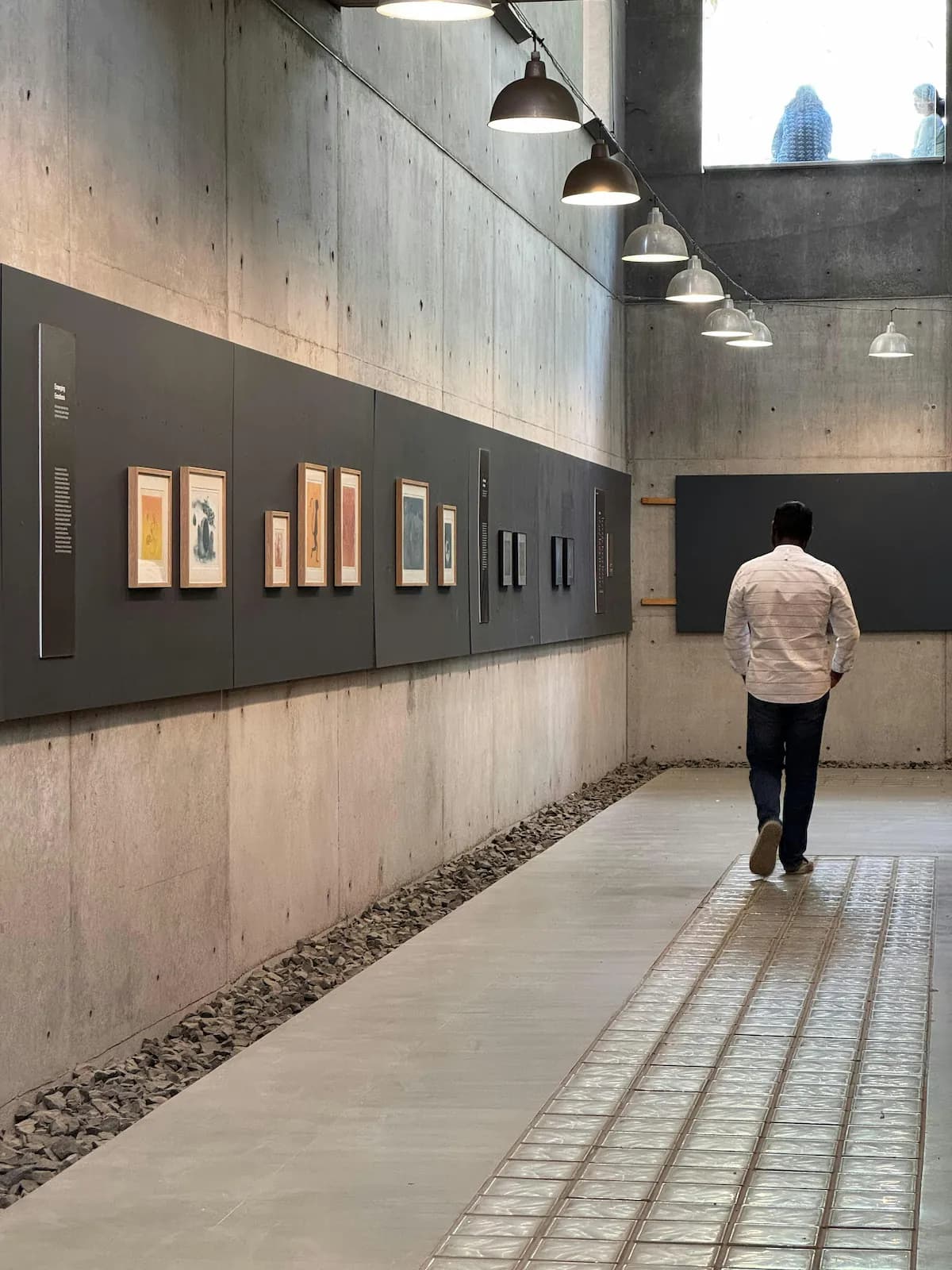 Un visiteur parcourt une longue salle de musée, le long d’œuvres encadrées.