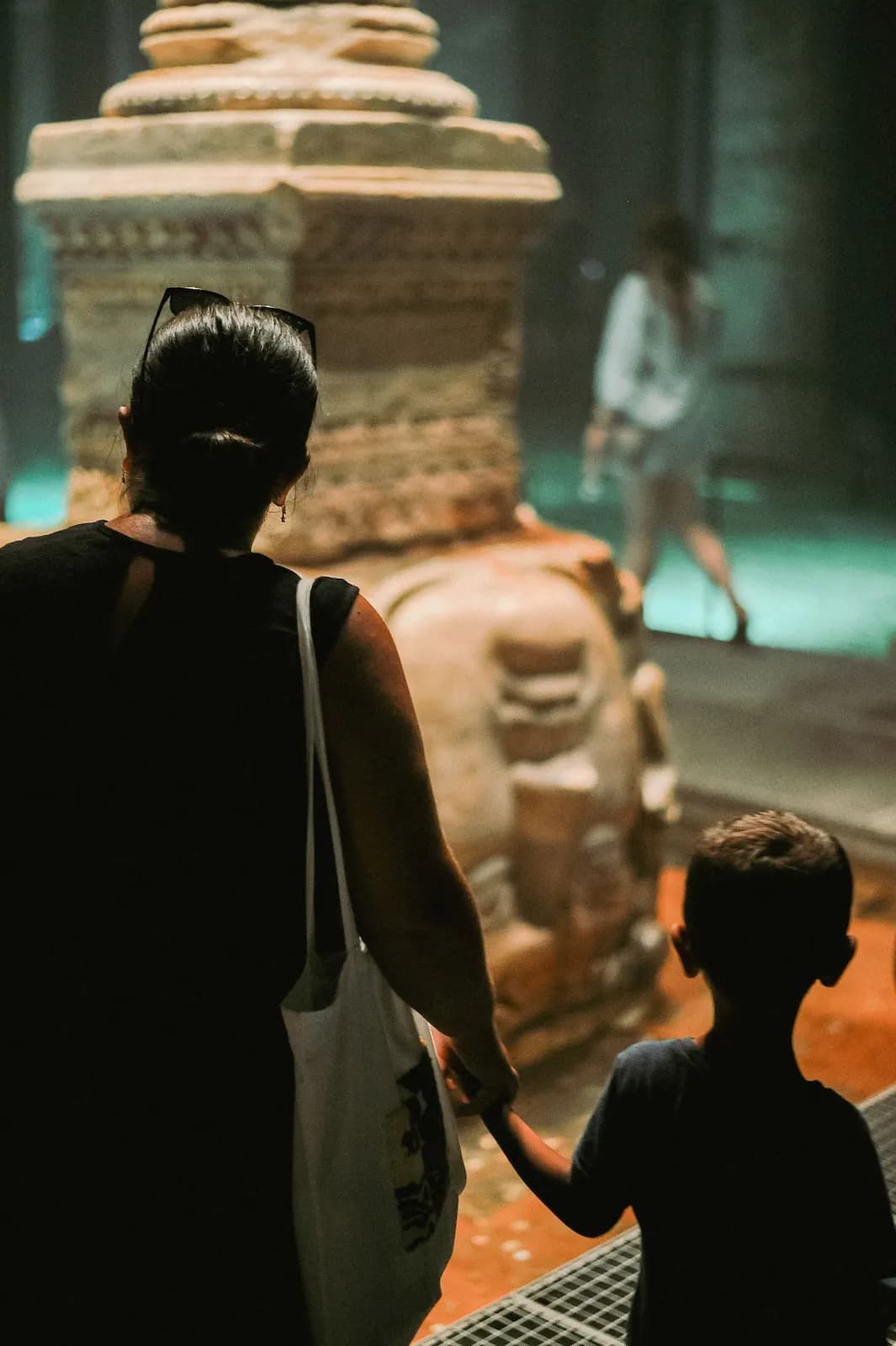 A mother and child, hand in hand, looking at a sculpture in a museum gallery.